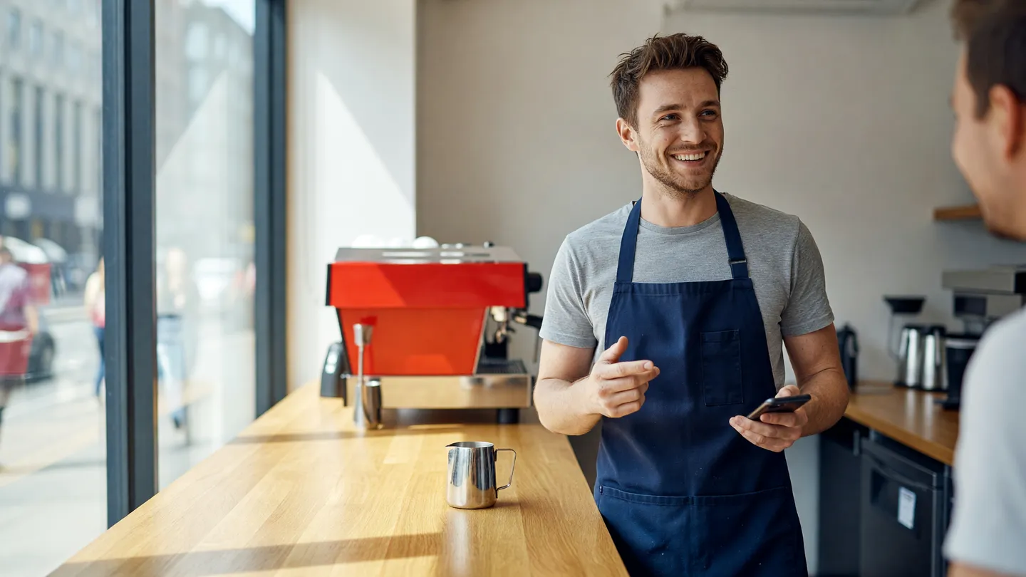 Barista risponde ai clienti in un locale luminoso, esempio di come gestire i commenti dopo le nuove funzioni social